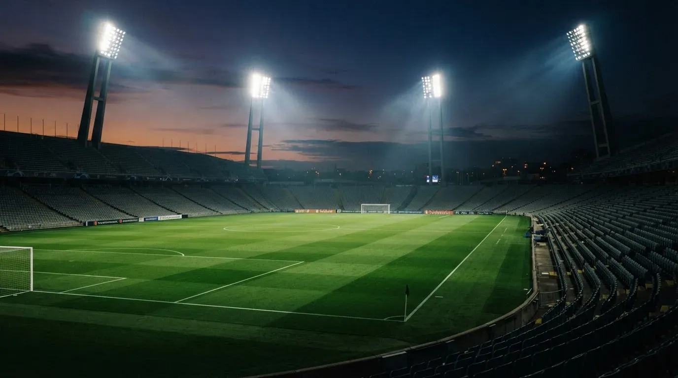 An empty football stadium with floodlight masts at dusk