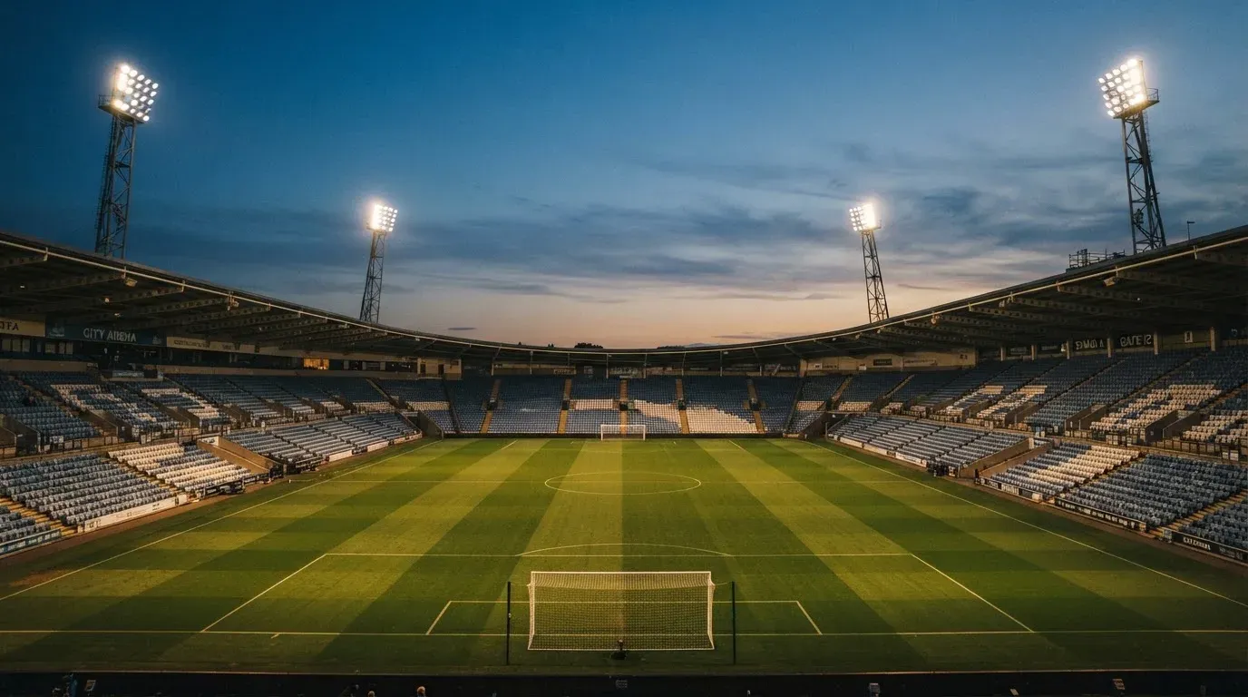 An empty football stadium with floodlight masts at dusk