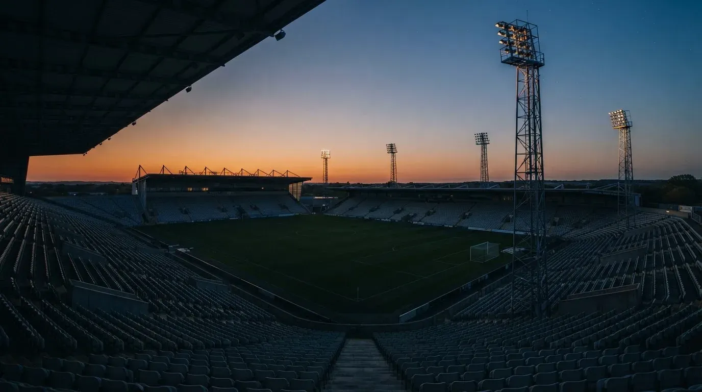 An empty football stadium with floodlight masts at dusk
