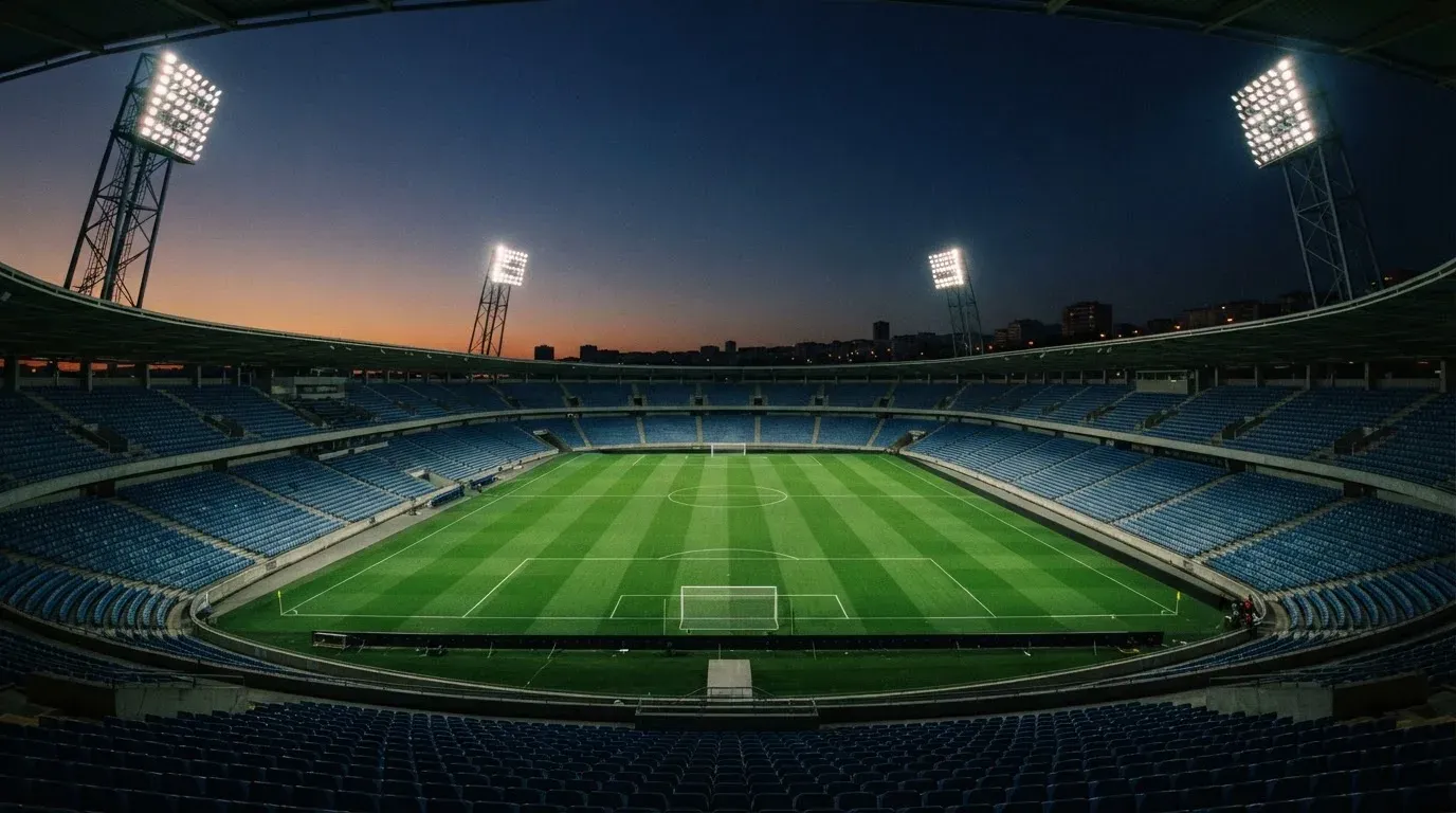 An empty football stadium with floodlight masts at dusk