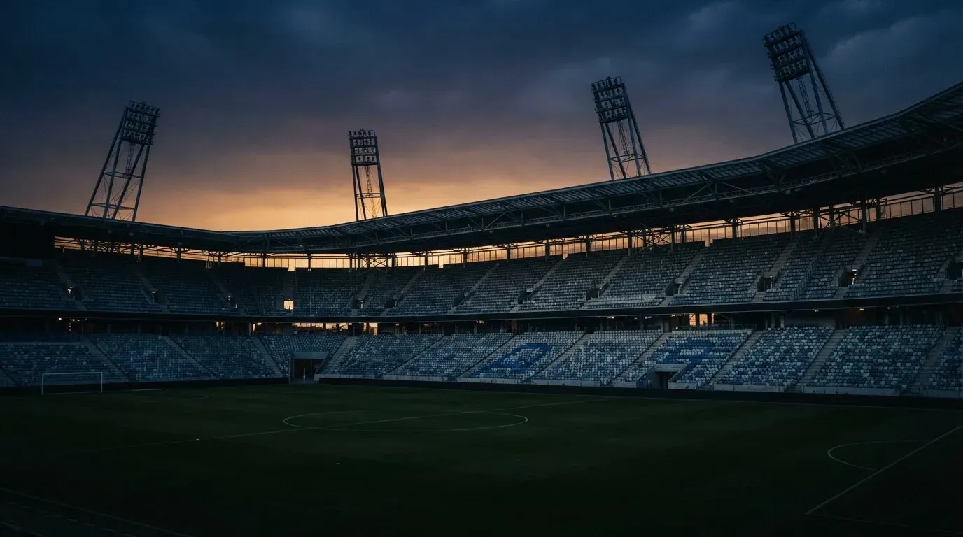 An empty football stadium with floodlight masts at dusk